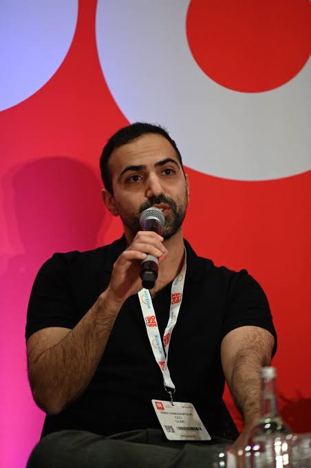 Amin Hamzianpour speaking on stage with a handheld microphone